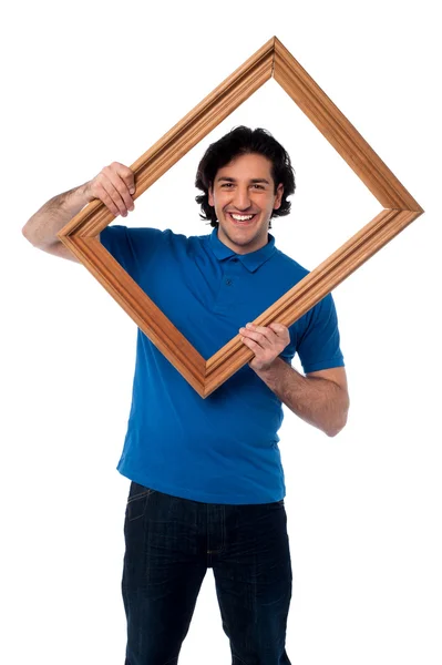 Smiling guy looking through picture frame — Stock Photo, Image