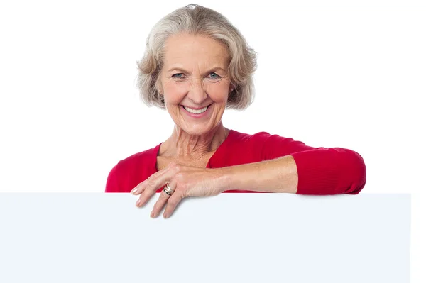 Mulher envelhecida em pé atrás de cartaz em branco — Fotografia de Stock