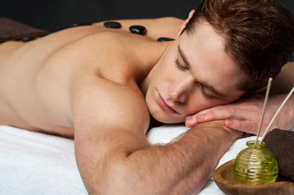 Homme relaxant sur un lit de massage aux pierres chaudes — Photo