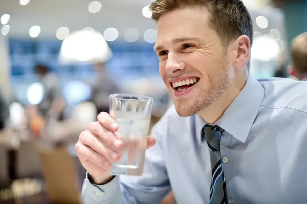 笑みを浮かべての若い男がカフェで水を飲む — ストック写真