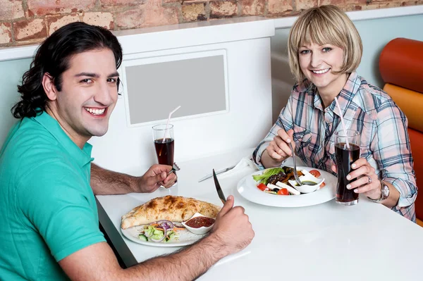 Jovem casal sorrindo desfrutando de refeições — Fotografia de Stock