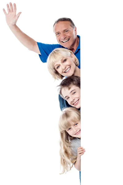 Joyful family of four behind blank whiteboard — Stock Photo, Image