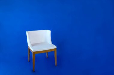 Mavi arka planda tahta bacaklı beyaz sandalye..