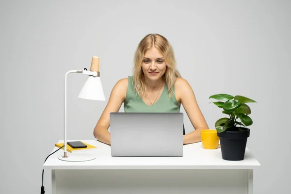 Portret pięknej młodej kobiety uczącej się przy stole z szarym laptopem, notatnikiem. Uśmiechnięta kobieta biznesu pracująca z laptopem odizolowanym na szarym tle. — Zdjęcie stockowe