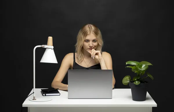 Retrato de una mujer joven y bonita estudiando mientras estaba sentada en la mesa con una computadora portátil gris, un cuaderno. Mujer de negocios sonriente trabajando con un portátil aislado sobre un fondo gris. — Foto de Stock