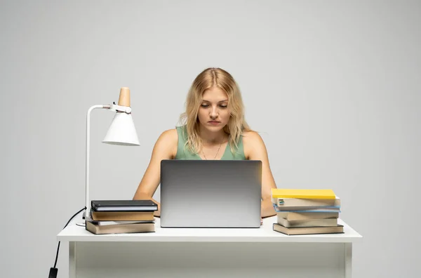Retrato de una mujer joven y bonita estudiando mientras estaba sentada en la mesa con una computadora portátil gris, un cuaderno. Mujer de negocios sonriente trabajando con un portátil aislado sobre un fondo gris. — Foto de Stock