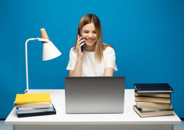 Masada oturan, dizüstü bilgisayarda çalışan ve telefonda müşterisiyle konuşan sarı saçlı çekici bir iş kadını. Akıllı bir telefonla konuşan neşeli bir öğrenci kız. Çalışıyorum.