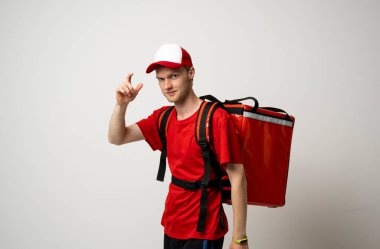 Renk arkaplanı termal çantalı genç kurye, mesaj için boşluk. Yemek dağıtım servisi. Kırmızı tişörtlü teslimatçı kurye olarak çalışıyor ve kırmızı termal yiyecek çantası tutuyor. Servis kavramı.