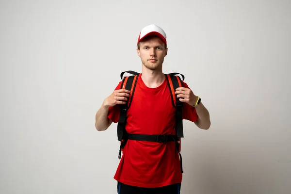 Młody kurier w czerwonym, mundurowym t-shircie z czerwoną torbą termo na ramieniu na białym tle. Usługi dostarczania żywności. — Zdjęcie stockowe