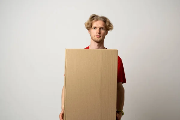 Delivery service. Young smiling courier holding cardboard box. Happy young delivery man in cap and red t-shirt standing with parcel isolated on white background.