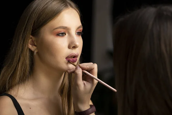 Makeup kunstner anvender rød læbestift på en smuk kvinde ansigt. Hånd make-up mester, maleri læber af unge skønhed model pige. Konfektion i processen. - Stock-foto