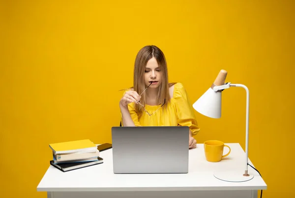 Retrato de estudio de la joven secretaria exitosa empleada mujer de negocios usar camiseta amarilla sentarse a trabajar en el escritorio de la oficina blanca con ordenador portátil navegar por Internet en línea aislado en el fondo amarillo. — Foto de Stock