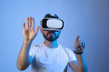 Sanal gerçeklik gözlüklü, neon ışıklı sakallı adam. Gelecekteki teknoloji konsepti. Genç adam VR gözlük takarken havaya dokunuyor..