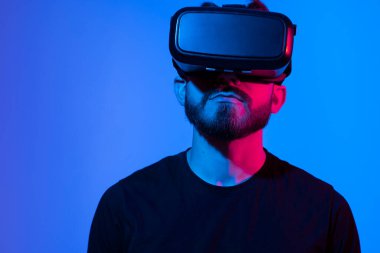 Sakallı adam metaevrenle etkileşim kurmak için kulaklık kaskı kullanıyor. Sanal gerçeklik 3D video izliyor. VR gözlüklü adam etrafa bakıyor..