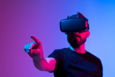 Şaşırmış genç sakallı adam, yüksek teknoloji ürünü VR gözlükler takıyor, 360 derecelik video izliyor ya da metaevrende video oyunu oynuyor..