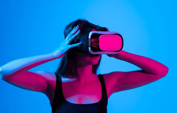 Chica alegre con las manos arriba usando las gafas de realidad virtual y jugando a un juego en luz de neón. Concepto de tecnología futura. Metaverso. — Foto de Stock