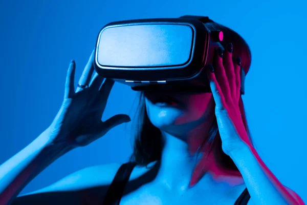 A fiatal nő VR fejhallgató sisakot használ, hogy kölcsönhatásba lépjen a metaverzióval, húzó és nyújtózkodó mozdulatokkal. Virtuális valóság megtekintése 3D-s videó. A lány VR szemüvegben körülnéz.. — Stock Fotó