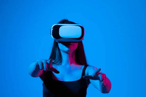 Chica alegre con las manos arriba usando las gafas de realidad virtual y jugando a un juego en luz de neón. Concepto de tecnología futura. Metaverso. — Foto de Stock