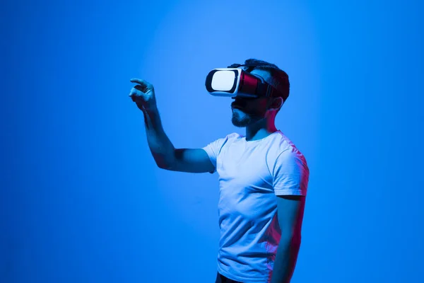 Retrato de hombre en camiseta negra con gafas de auriculares 3D haciendo gestos como si tocara algo de lo que hace en realidad virtual mientras juega a videojuegos. Metaverso. — Foto de Stock