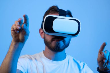 Üç boyutlu gözlüklerle video oyunu oynayan yakışıklı bir adamın portresi. Sanal gerçeklik kulaklığı takan oyuncu kafasına akıllı telefon takıyor ve gülümsüyor..