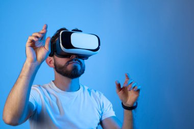 Sakallı adam metaevrenle etkileşim kurmak için kulaklık kaskı kullanıyor. Sanal gerçeklik 3D video izliyor. VR gözlüklü adam etrafa bakıyor..