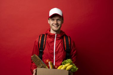 Kırmızı üniformalı bir teslimatçı omzunda termal torbayla evdeki müşteriye yemek getiriyor. Çevrimiçi market alışveriş hizmeti kavramı.