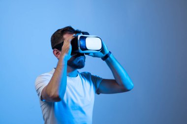 Siyah tişörtlü çekici genç adam sanal gerçeklik kulaklığı ya da 3D gözlük takıyor. Video oyunu oynayan ve VR kulaklık kullanan yakışıklı bir erkek..