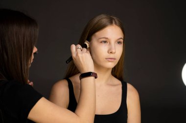 Makyaj yapma işlemi. Fırça ile çalışma modeli yüzünde makyaj sanatçısı. Güzellik Salonu iç sarışın genç kadın portresi. Cilde uygulanan sesi.