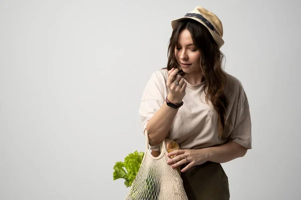 Mujer feliz en una camiseta beige y un sombrero con bolsa de compras de algodón reutilizable con comestibles, pan y verduras. Concepto de no plástico. Cero residuos, sin plástico. Estilo de vida sostenible. — Foto de Stock