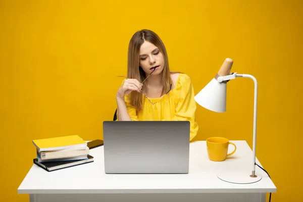 Retrato de estudio de la joven secretaria exitosa empleada mujer de negocios usar camiseta amarilla sentarse a trabajar en el escritorio de la oficina blanca con ordenador portátil navegar por Internet en línea aislado en el fondo amarillo. — Foto de Stock