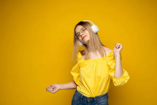 Chica feliz en gafas y camisa amarilla bailando y escuchando la música aislada sobre un fondo amarillo. —  Fotos de Stock