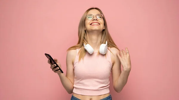 Photo rapprochée d'une jolie jeune femme blonde riante et positive portant une chemise jaune élégante et des lunettes communiquant sur un téléphone portable et souriant isolé sur fond jaune. — Photo