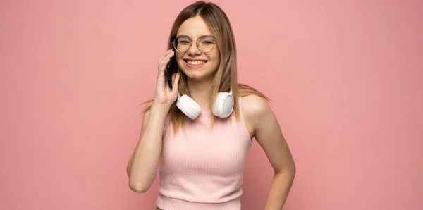 Portré egy aranyos boldog lány sárga ing és szemüveg egy fejhallgató a nyakon beszél a mobiltelefon és nevetés elszigetelt sárga háttér. — Stock Fotó