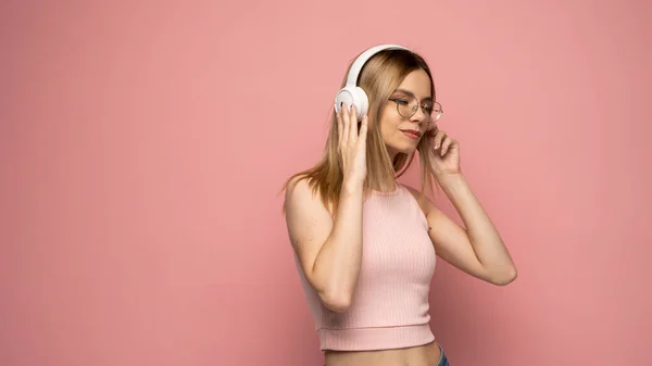 Chica feliz en gafas y camisa rosa bailando y escuchando la música aislada sobre un fondo rosa. —  Fotos de Stock