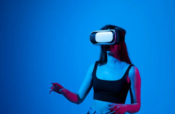 Retrato de una joven jugando en gafas VR con luz de neón sobre fondo azul. Concepto de aparatos y tecnologías modernas. Concepto de tecnología futura. Juego de realidad virtual. — Foto de Stock
