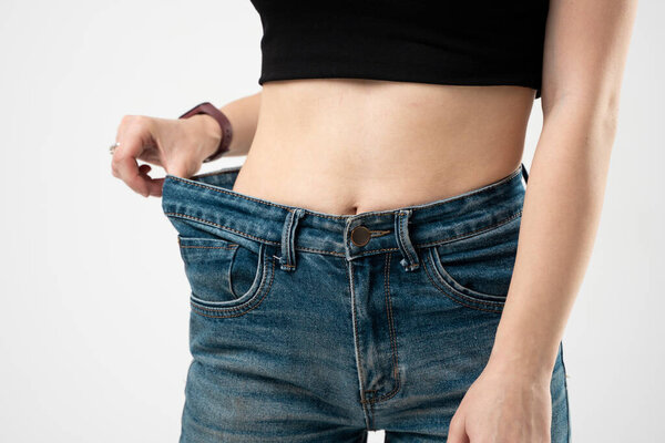 Diet concept and weight loss. Woman in oversize jeans on white background.