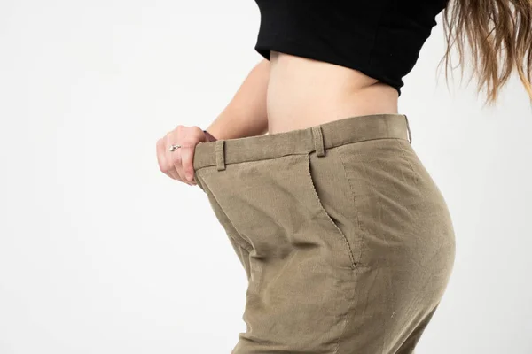 灰色の背景に古いジーンズを着て減量後の結果を示す女性。ダイエットの概念と減量. — ストック写真