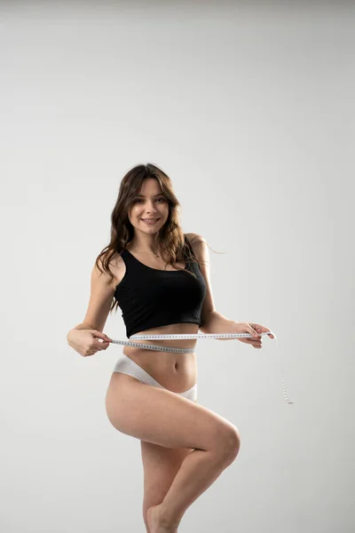 スリムな若い女性は白い背景に隔離されたセンチメートルのテープメジャーで彼女の細い腰を測定します。スポーティ女性スリムフィギュアライフスタイルモチベーションワークアウト. — ストック写真