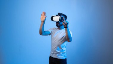 Meta evren konsepti. VR gözlüklü Avrupalı genç adam, sanal gerçeklik kulaklığıyla video oyunları oynuyor, elle bir şeye dokunmaya çalışıyor..