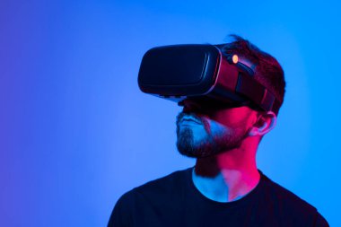 VR kulaklık kullanan bir adamın portresi karanlık bir iç aydınlatma aydınlatmasıyla video oyunu oynarken. Renkli ışık ile yakın plan gelecekçi Google 'lar.