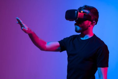 Karanlık iç aydınlatmalı neon ışıkta metaevrende bir arkadaşla iletişim kurarken VR kulaklık kullanan bir adamın portresi. Renkli ışık ile yakın plan gelecekçi Google 'lar.