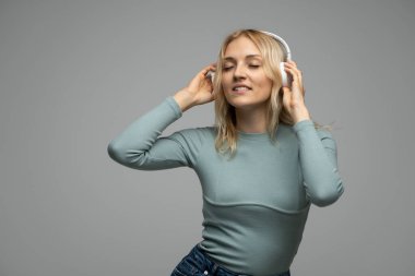 Güzel dans eden genç bir kadın koyu gri arka planda kablosuz kulaklıkla müzik dinliyor..