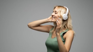 Gri arka planda kulaklıkla müzik dinleyen güzel genç bir kadın..