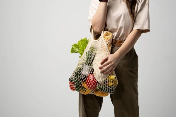 Mano femenina con bolsa eco de malla con comestibles sobre fondo gris. Concepto de cero residuos. —  Fotos de Stock