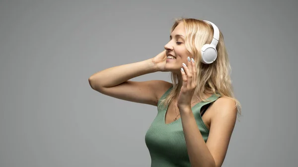 Schöne junge Frau hört Musik mit Kopfhörern auf grauem Hintergrund. — Stockfoto
