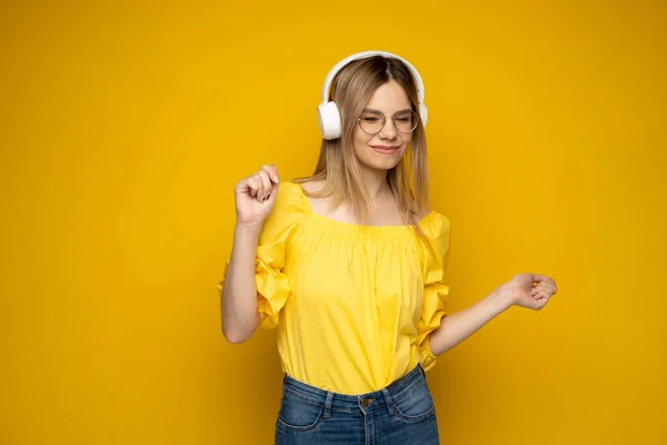 Chica feliz en gafas y camisa amarilla bailando y escuchando la música aislada sobre un fondo amarillo. —  Fotos de Stock