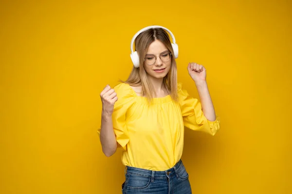 Concepto de estilo de vida. Retrato de una hermosa mujer con gafas y camisa amarilla alegre escuchando música. Fondo amarillo del estudio. Copiar espacio. —  Fotos de Stock