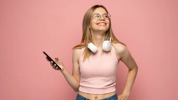 Jeune femme blonde en lunettes et t-shirt rose sur fond rose isolé envoyant un message avec le mobile. — Photo