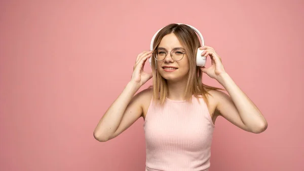Belle jeune femme blonde avec écouteurs et appareil mobile écoutant de la musique et souriant et dansant, isolé sur fond rose. — Photo