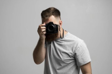 Gri tişörtlü profesyonel fotoğrafçının portresi fotoğraf makinesine bakıyor ve gri arkaplanda fotoğraf çekimi yapıyor..